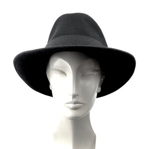 Op de afbeelding: Een zwarte fedora-hoed met een brede rand, die op een wit mannequins hoofd zit.