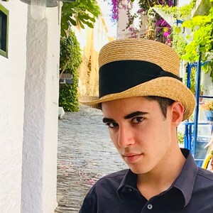 Peut inclure: Un jeune portant une chemise &agrave; col noir et un chapeau de paille &agrave; bords larges avec un bandeau noir. Le chapeau a une couronne haute.