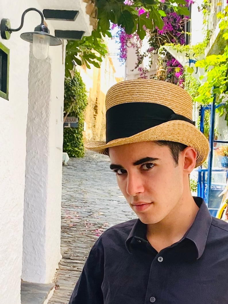 Peut inclure: Un jeune portant une chemise &agrave; col noir et un chapeau de paille &agrave; bords larges avec un bandeau noir. Le chapeau a une couronne haute.