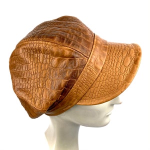 May include: A brown leather cap with a crocodile-embossed pattern. The cap has a curved brim and a flat top.