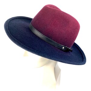 May include: A burgundy felt fedora with a wide brim and a black leather band. The brim is turned down on one side.