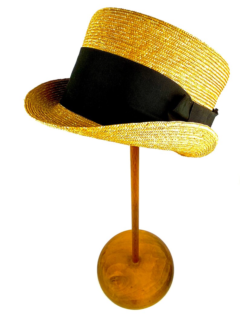 Peut inclure: Un chapeau de paille avec un ruban noir et un n&oelig;ud. Le chapeau est sur un support en bois.