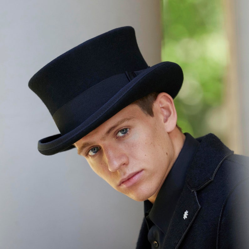 May include: A black top hat with a black band. The hat is worn by a person with short brown hair.