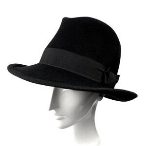 Op de afbeelding: Een zwarte fedora hoed met een brede rand en een zwart lint.
