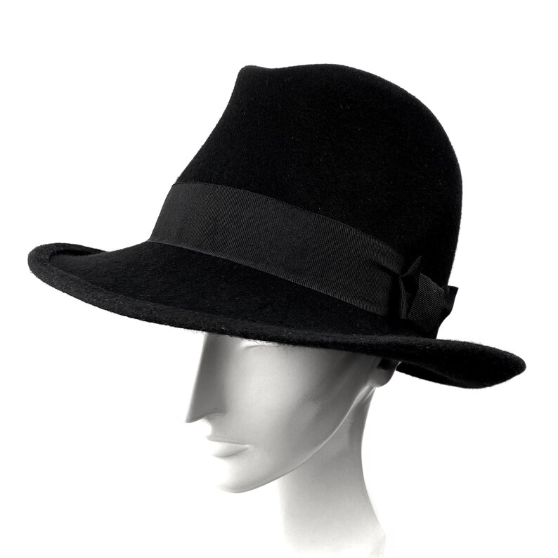 Op de afbeelding: Een zwarte fedora hoed met een brede rand en een zwart lint.