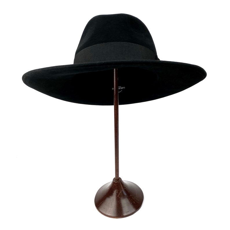 K&ouml;nnte beinhalten: Ein schwarzer Fedora-Hut mit breiter Krempe, der auf einem braunen St&auml;nder steht.