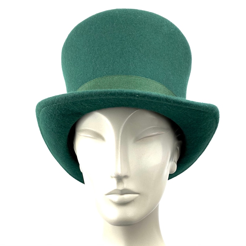 May include: A green top hat with a black band. The hat is sitting on a white mannequin head.