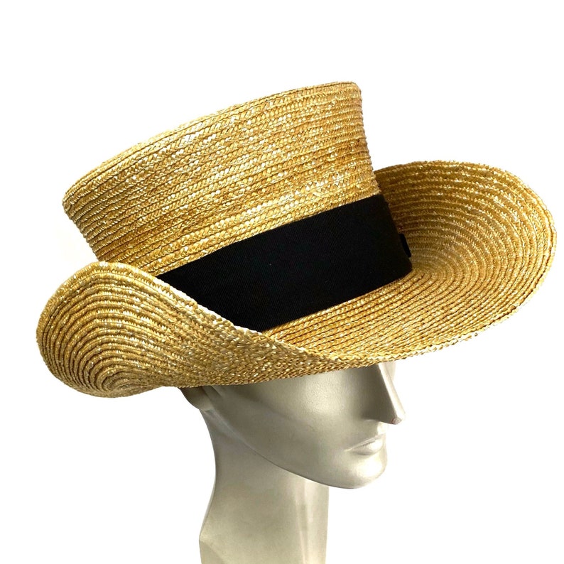 Pu&ograve; includere: Un cappello di paglia a tesa larga e un nastro nero attorno alla corona. Il cappello &egrave; fatto di un materiale intrecciato ed &egrave; di colore marrone chiaro.