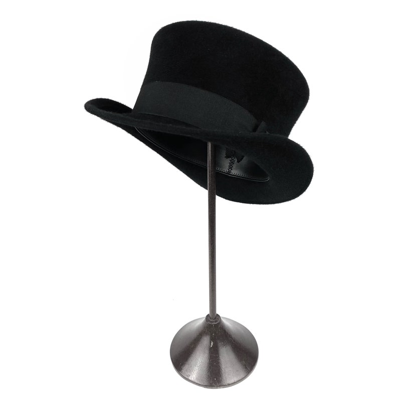 Peut inclure: Un chapeau haut de forme noir avec un bandeau noir pos&eacute; sur un support en m&eacute;tal noir. Le chapeau est en feutre et a une finition lisse.