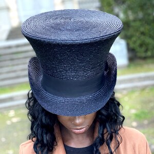 以下が含まれることがあります： 黒いストローで編まれたトップハットで、黒いリボンが付いています。帽子は高く、つばが広いです。