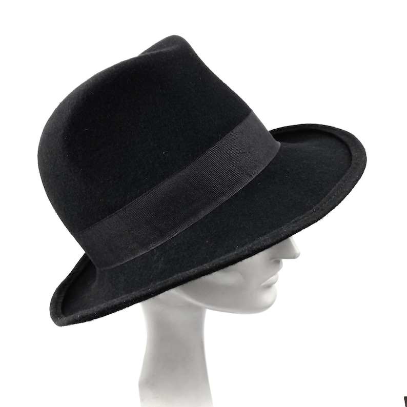 Op de afbeelding: Een zwarte fedora hoed met een brede rand en een zwarte band.