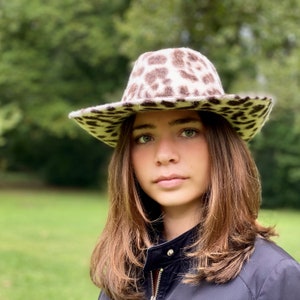 May include: A young person wearing a black jacket with a brown and white leopard print cowboy hat.