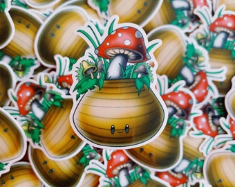 May include: A collection of stickers featuring a cartoon mushroom design. The central sticker shows a smiling, brown pot with a red-capped mushroom and smaller mushrooms emerging from it. Green leaves and grass surround the mushrooms.