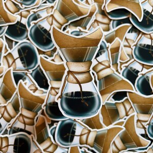 May include: A close-up of a sticker featuring a hand-drawn illustration of a coffee maker with a brown filter and a dark brown glass carafe. The sticker is surrounded by other stickers of the same design.