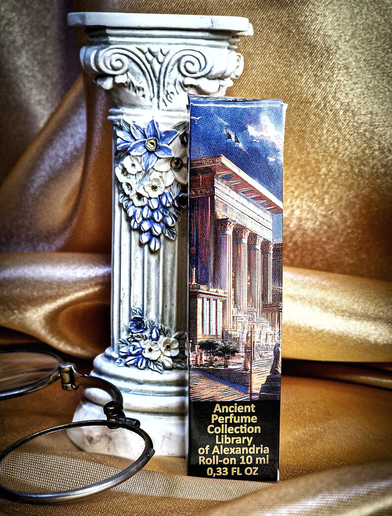 May include: A decorative white column with blue and white floral accents stands next to a perfume box. The box features an illustration of an ancient building and reads "Ancient Perfume Collection Library of Alexandria Roll-on 10 ml 0.33 FL OZ."