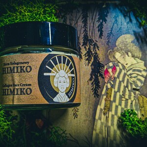 以下が含まれることがあります： 「Krem Kolagenowy HIMIKO Collagen Face Cream HIMIKO」と金色に書かれたラベルが貼られた茶色の瓶。瓶は緑色の苔むした表面に置かれ、その前にヴィンテージの日本の絵画が飾られている。