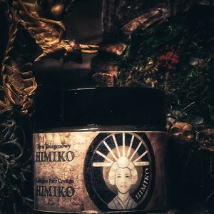 以下が含まれることがあります： 「Irm Kolagenowy HIMIKO Collagen Face Cream HIMIKO」と金色に書かれたラベルが付いた、濃い茶色の瓶。ラベルには、伝統的な日本の着物姿の女性が、日の丸を背負って描かれた白黒のイラストが描かれている。