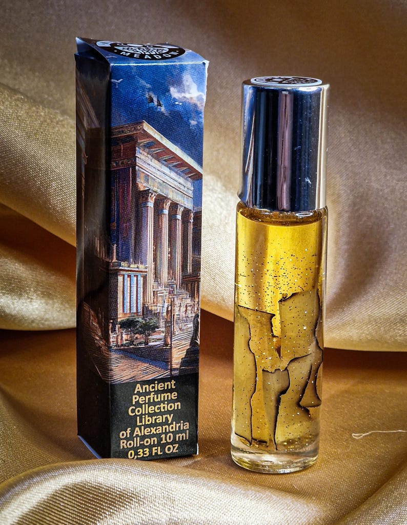 May include: A roll-on perfume bottle and its box. The bottle is clear with a silver cap, filled with a golden liquid and decorative elements. The box features an illustration of an ancient building and text that reads "Ancient Perfume Collection Library of Alexandria Roll-on 10 ml 0.33 FL OZ."