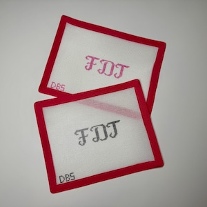 May include: Two square needlepoint canvases with red borders. One canvas has pink embroidered initials "FDJ", the other has black embroidered initials. The letters "DBS" are embroidered in the lower left corner of each canvas.
