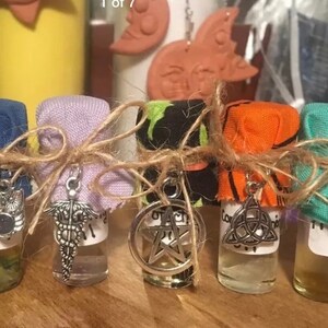 May include: Seven small glass bottles with different colored fabric coverings and charms. Each bottle contains a clear liquid and has a label that says "Oil".