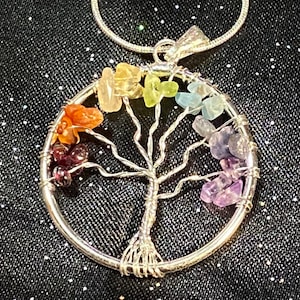 May include: A silver chain necklace with a wire-wrapped tree of life pendant. The tree is adorned with colourful gemstones in a rainbow pattern.