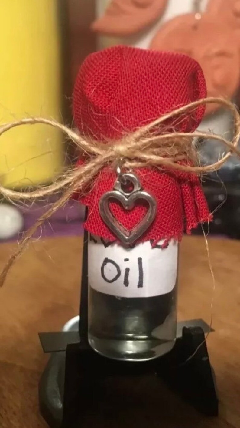 May include: A small glass bottle with a red fabric cover tied with twine and a silver heart charm. The bottle is labeled "oil".