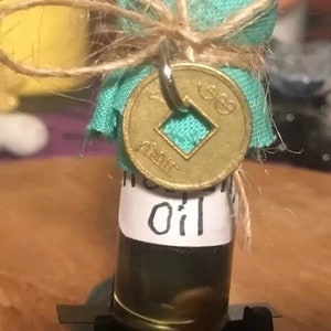May include: A small glass bottle with a teal fabric cover tied with twine and a gold coin charm. The bottle contains a dark liquid and has a white label that reads "Incense Oil".