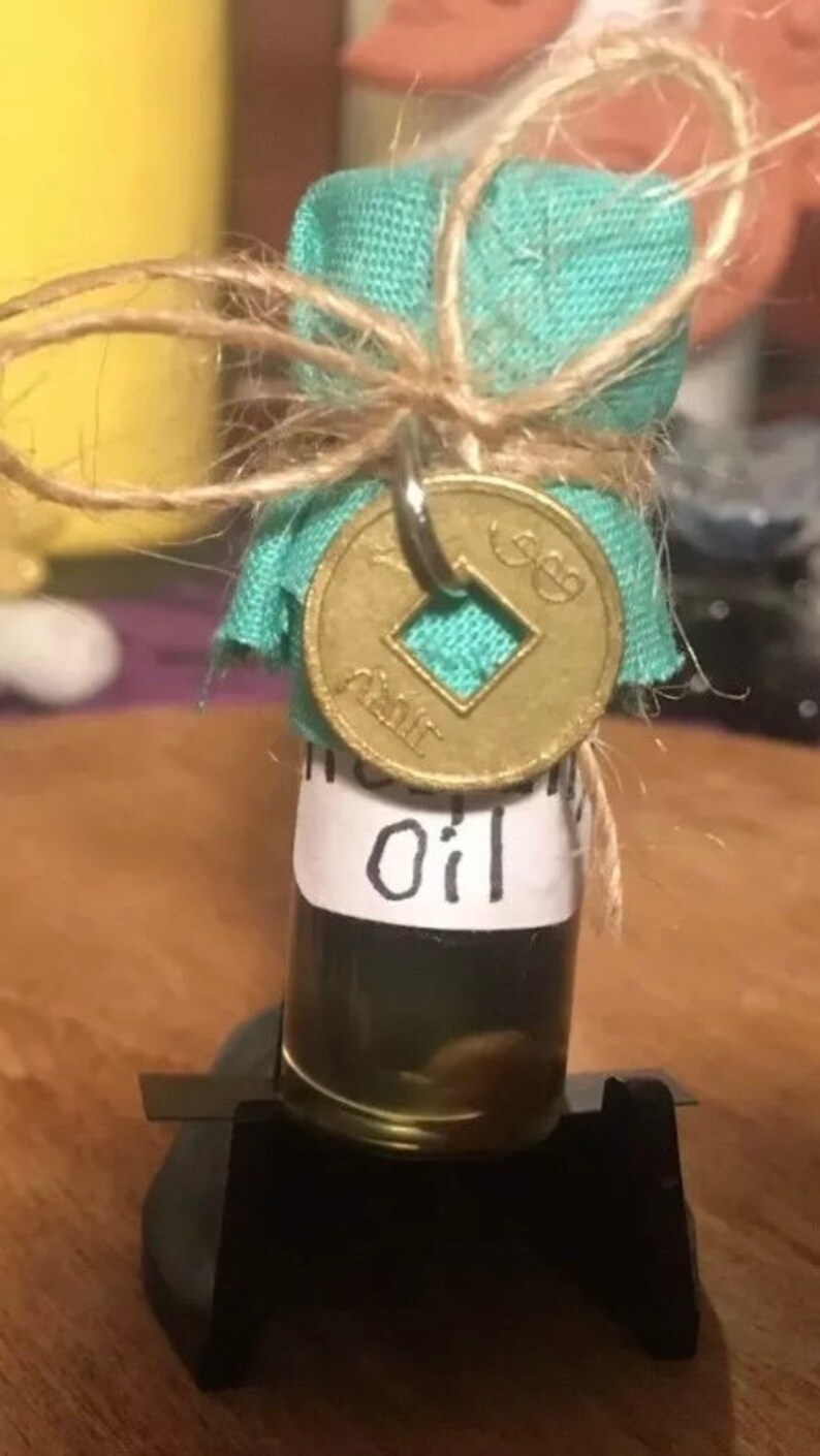 May include: A small glass bottle with a teal fabric cover tied with twine and a gold coin charm. The bottle contains a dark liquid and has a white label that reads "Incense Oil".