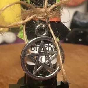 May include: A small glass bottle with a black and green fabric cover tied with twine. The bottle has a silver pendant with a pentagram charm and the word "protection" written on the label.