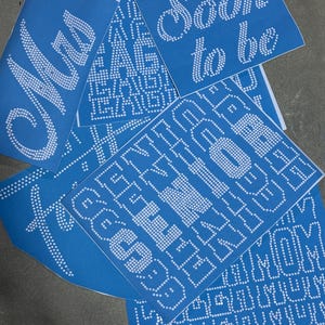 May include: A collection of blue transfer sheets featuring white rhinestone designs. The sheets display text including "Mrs", "Soon to be", and "SENIOR 2024", along with various alphabet letters arranged in rows, all created with small circular dots.