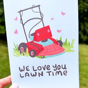 May include: A light blue card with a cartoon illustration of a red lawnmower with a happy face. The lawnmower is surrounded by green grass and pink hearts. The text "WE LOVE YOU LAWN TIME" is written in black at the bottom of the card.