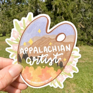 May include: A sticker featuring a paint palette with a mountain scene and the text "Appalachian artist" in a brown, white, and green color scheme. The sticker is surrounded by a floral border and includes the website "www.jammfoundation.com".
