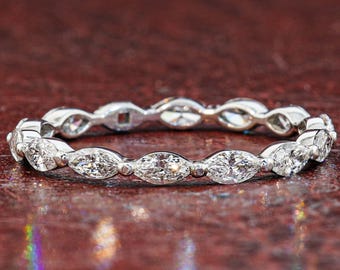 Puede incluir: Una alianza de color plateado con una hilera continua de piedras transparentes de talla marquesa engastadas en un marco de metal. El anillo muestra un patrón repetitivo de gemas alargadas y puntiagudas aseguradas por pequeñas garras metálicas.