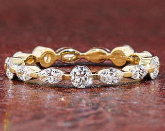 May include: A gold eternity band featuring an alternating pattern of round brilliant-cut and marquise-cut clear gemstones. The ring is crafted with a polished gold metal setting that secures each stone in a shared prong or bezel-style arrangement.