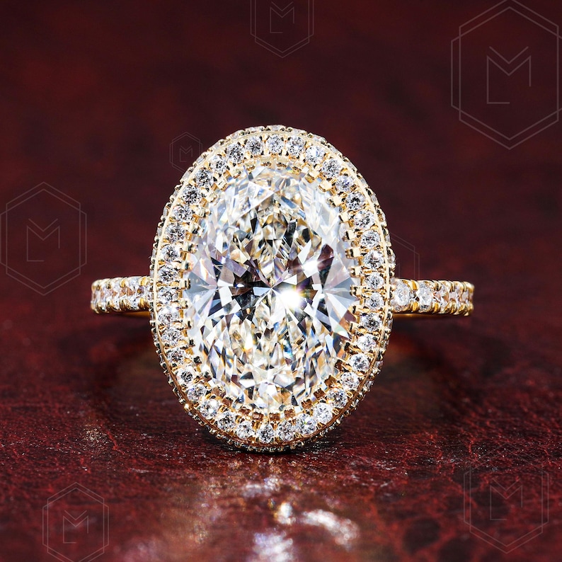 May include: A gold engagement ring with a large oval-shaped diamond surrounded by a double halo of smaller diamonds.