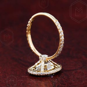 May include: A gold engagement ring with a large, clear, square-shaped diamond set in a halo of smaller diamonds. The band is also set with smaller diamonds.