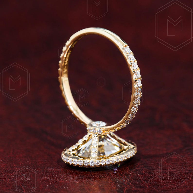 May include: A gold engagement ring with a large, clear, square-shaped diamond set in a halo of smaller diamonds. The band is also set with smaller diamonds.