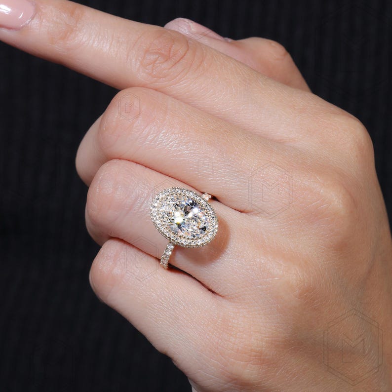 May include: A gold ring with a large oval-shaped diamond surrounded by a halo of smaller diamonds. The ring has a pave setting with smaller diamonds on the band.