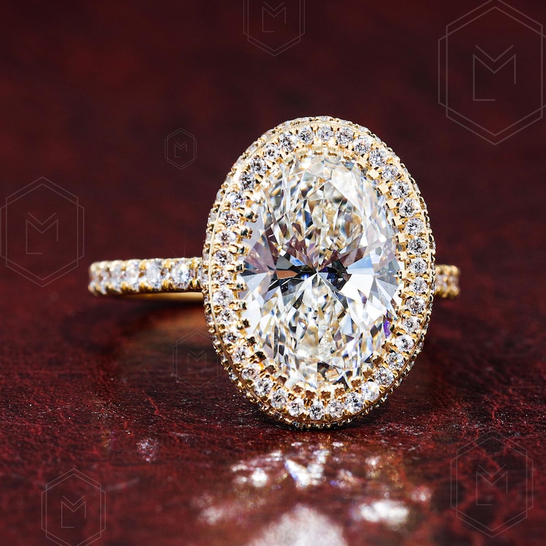 May include: A gold engagement ring with a large oval-shaped diamond surrounded by a double halo of smaller diamonds.
