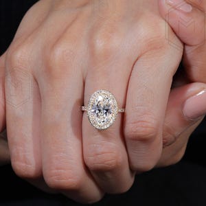 May include: A gold engagement ring with a large oval-shaped center diamond surrounded by a double halo of smaller diamonds.