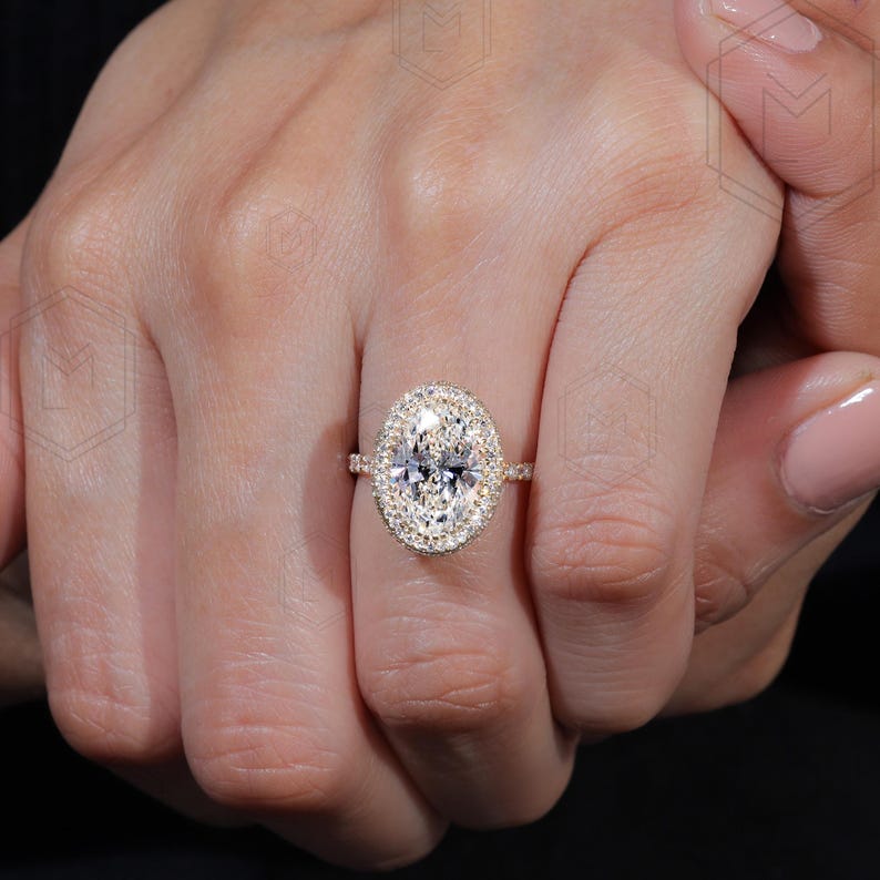 May include: A gold engagement ring with a large oval-shaped center diamond surrounded by a double halo of smaller diamonds.