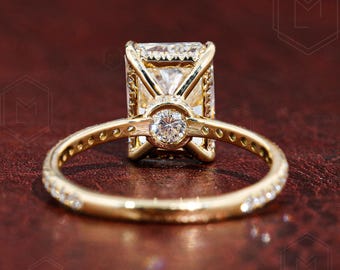 Könnte beinhalten: Ein goldener Verlobungsring mit einem großen Smaragdschliff-Diamanten, der in einer Pavé-Fassung sitzt. Die Ringschiene ist ebenfalls mit kleineren Diamanten in Pavé-Fassung besetzt.
