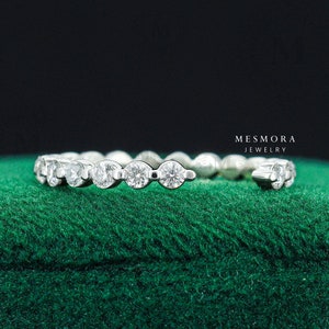 May include: A silver band ring with a row of round, clear gemstones. The ring is on a green velvet surface.