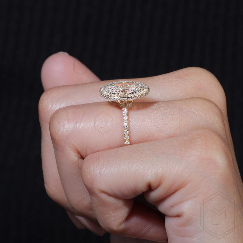 May include: A gold ring with a large oval-shaped diamond surrounded by smaller diamonds. The ring is set on a thin band with smaller diamonds.