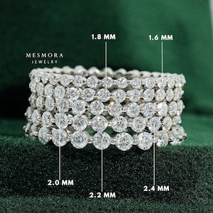Op de afbeelding: Een stapel van vijf zilverkleurige eternity-ringen met ronde, heldere stenen. De afbeelding bevat tekstlabels die de steenmaten van 1,6 mm, 1,8 mm, 2,0 mm, 2,2 mm en 2,4 mm aangeven, samen met de merknaam Mesmora Jewelry in witte letters.