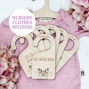 Puede incluir: Separadores de ropa de guardería de madera con el texto "Nursery Clothes Dividers" en un círculo. Los separadores están etiquetados como "Newborn", "0-3 Months", "6-9", "9-12" y "18-24". Los separadores están sobre un body rosa.