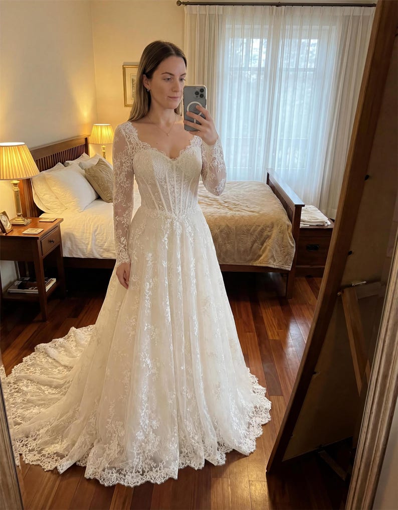 May include: A floor-length white wedding dress featuring long lace sleeves, a sweetheart neckline, and a structured corset-style bodice. The gown is adorned with intricate floral lace embroidery throughout, flowing into a full skirt with a train.