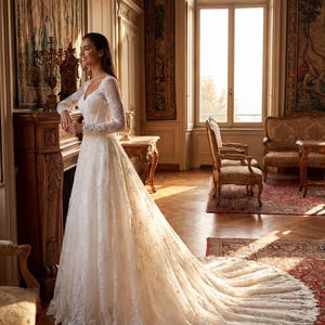 May include: A floor-length white wedding dress featuring long lace sleeves, a V-neckline, and a fitted bodice that transitions into a full, flowing skirt with an extended train. The entire garment is covered in intricate floral lace detailing.