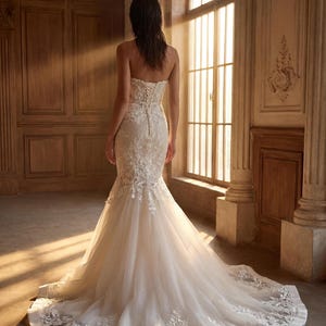 May include: A strapless ivory wedding dress featuring a fitted bodice with intricate floral lace embroidery, a corset-style lace-up back, and a flared mermaid skirt that extends into a long train with matching lace detailing along the hemline.
