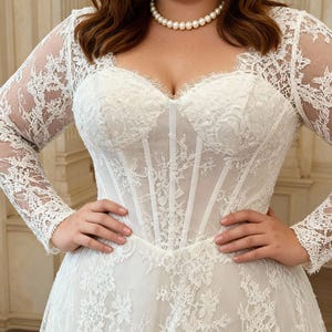 May include: A white floor-length gown featuring a sweetheart neckline, a structured corset-style bodice with vertical boning, and long sheer lace sleeves. The dress is adorned with intricate floral lace overlays and a full skirt with lace detailing.